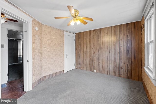 unfurnished room with wooden walls, ceiling fan, and dark colored carpet