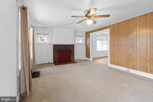 unfurnished living room with a brick fireplace, light colored carpet, ceiling fan, and wood walls