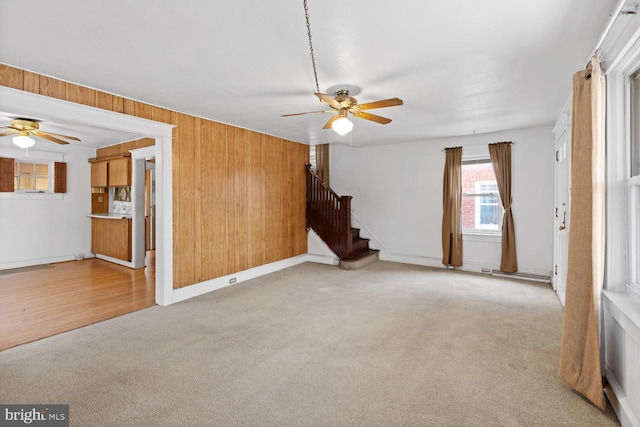 unfurnished living room with light carpet, ceiling fan, and wood walls