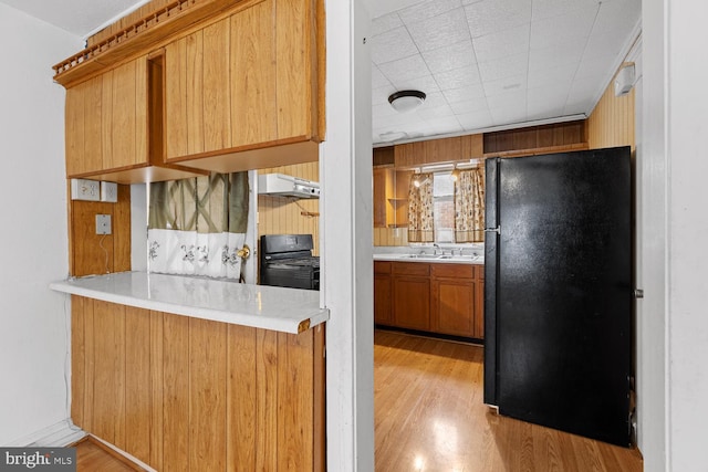 kitchen featuring sink, range, black refrigerator, kitchen peninsula, and light wood-type flooring