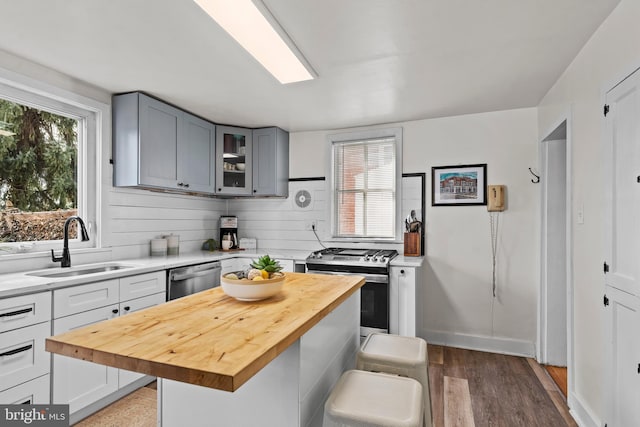 kitchen with stainless steel appliances, butcher block counters, a sink, a center island, and glass insert cabinets