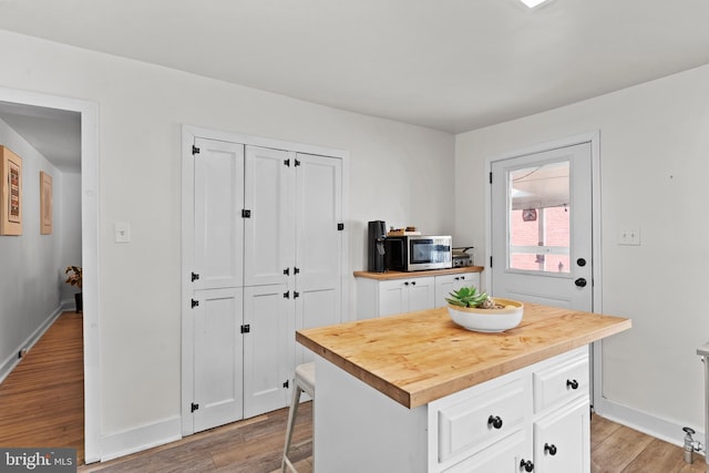 kitchen featuring a kitchen island, white cabinetry, wooden counters, light wood-type flooring, and stainless steel microwave