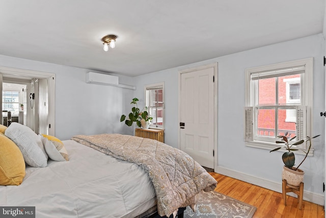 bedroom with light wood-style flooring, baseboards, radiator heating unit, and an AC wall unit