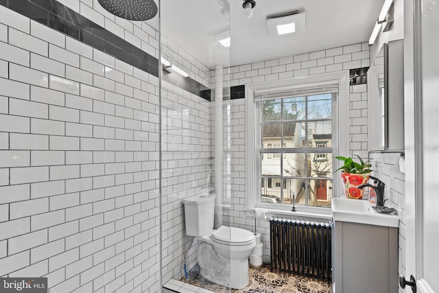 bathroom featuring radiator, a tile shower, tile walls, and vanity