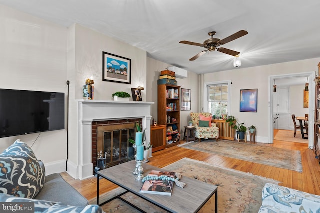 living room featuring a ceiling fan, baseboards, a fireplace, and light wood finished floors