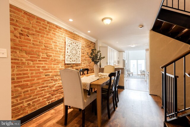 dining room with dark wood-type flooring, brick wall, and stairs