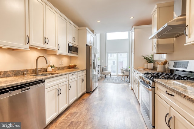 kitchen with wall chimney exhaust hood, stainless steel appliances, light wood-type flooring, a sink, and recessed lighting