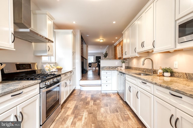 kitchen with stainless steel appliances, a sink, white cabinetry, light wood-type flooring, and wall chimney exhaust hood