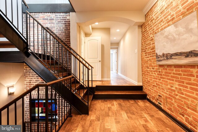 stairway featuring arched walkways, recessed lighting, brick wall, wood finished floors, and baseboards