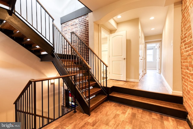 stairway featuring brick wall, baseboards, wood finished floors, and recessed lighting