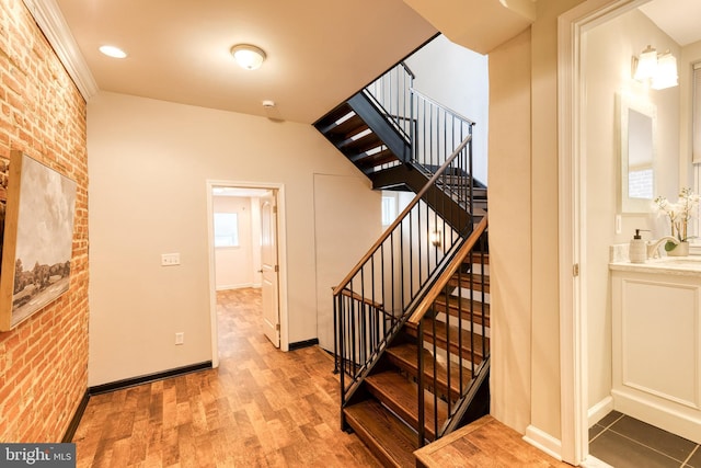 stairway featuring baseboards, brick wall, and wood finished floors