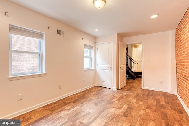 unfurnished room with brick wall, visible vents, baseboards, stairs, and light wood-style floors