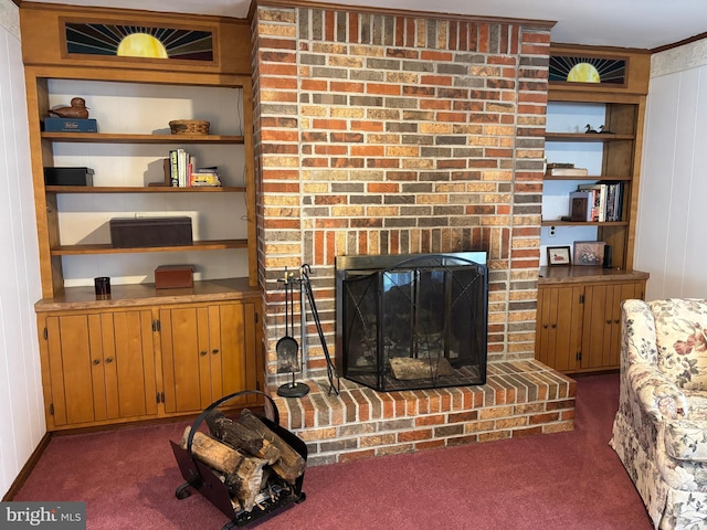 living area featuring built in shelves, a fireplace, dark carpet, and crown molding