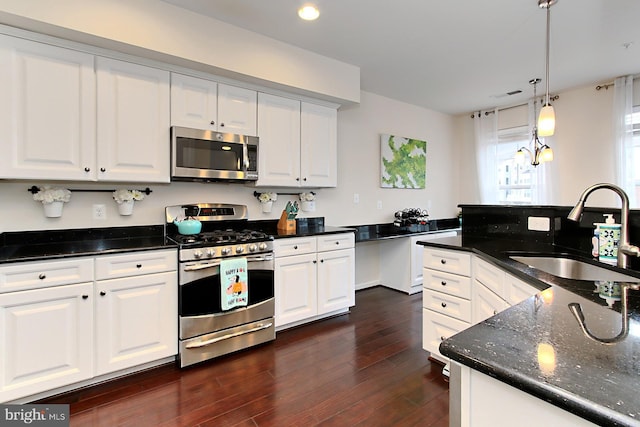 kitchen featuring sink, hanging light fixtures, stainless steel appliances, white cabinets, and dark stone counters