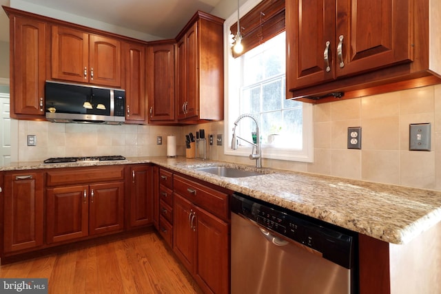 kitchen with stainless steel appliances, light stone counters, light wood-type flooring, and a sink