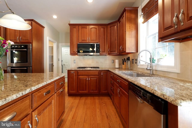 kitchen featuring light stone counters, stainless steel appliances, a sink, decorative backsplash, and decorative light fixtures