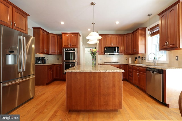 kitchen featuring a center island, pendant lighting, light wood finished floors, appliances with stainless steel finishes, and a sink