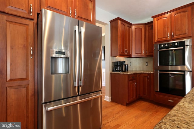 kitchen with stainless steel appliances, light wood finished floors, decorative backsplash, and light stone countertops