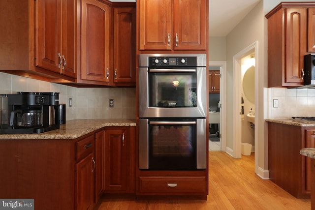 kitchen featuring light stone counters, brown cabinets, stainless steel appliances, tasteful backsplash, and light wood-style flooring