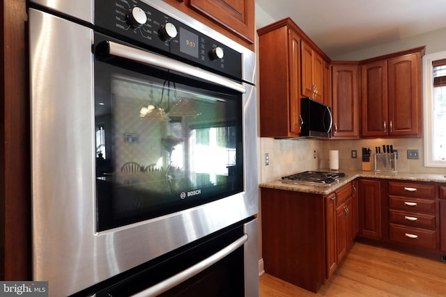 kitchen featuring light stone countertops, stainless steel appliances, brown cabinets, light wood finished floors, and tasteful backsplash