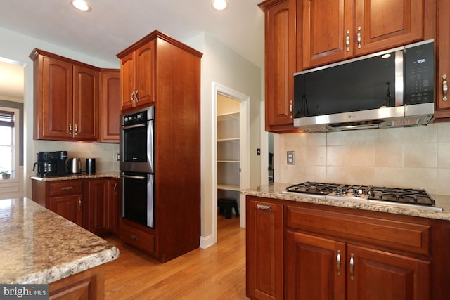 kitchen with light stone counters, recessed lighting, stainless steel appliances, light wood-style floors, and brown cabinets