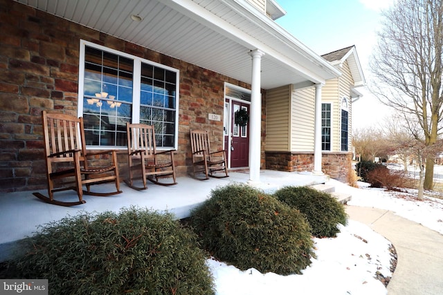 snow covered property entrance with covered porch and stone siding