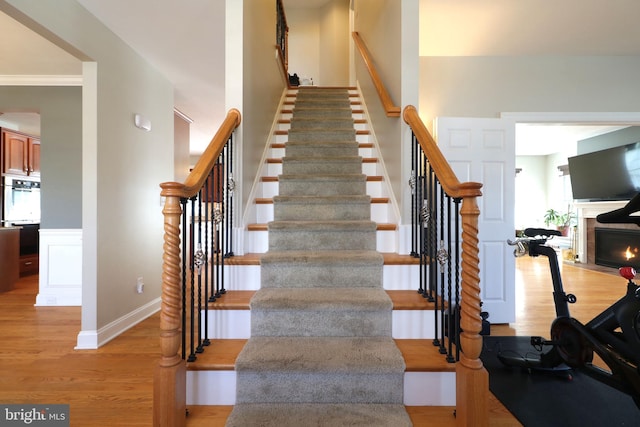 staircase featuring a fireplace with flush hearth, a decorative wall, wood finished floors, and wainscoting