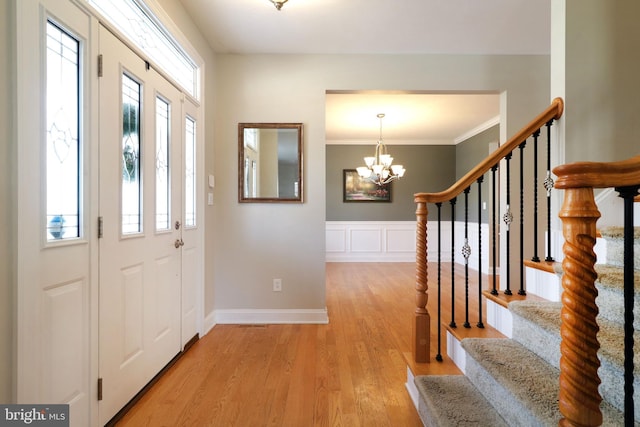 foyer entrance with a notable chandelier, a wainscoted wall, light wood-style floors, stairway, and crown molding