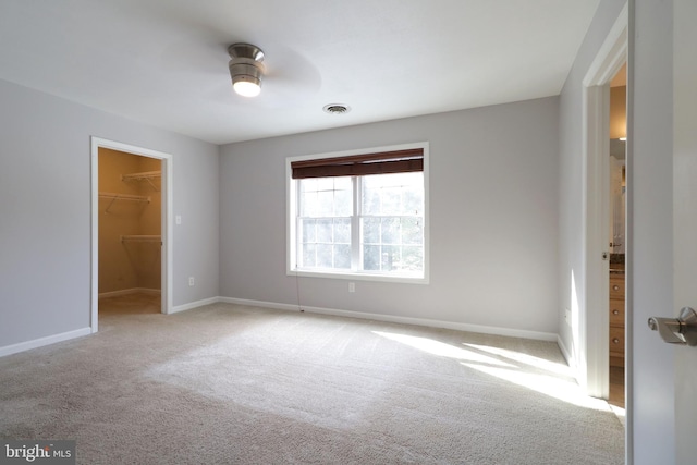 unfurnished bedroom featuring a closet, light colored carpet, visible vents, a spacious closet, and baseboards