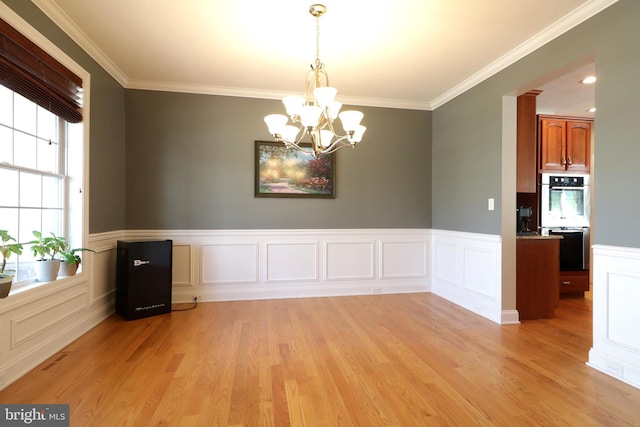 unfurnished dining area featuring ornamental molding, a notable chandelier, and light wood finished floors