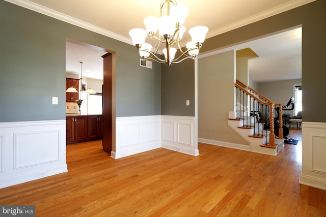 unfurnished dining area featuring light wood-style floors, a wainscoted wall, crown molding, and stairway