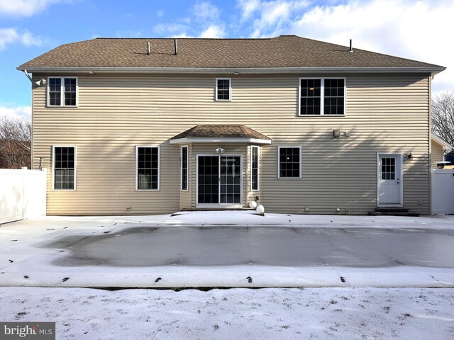 snow covered house with roof with shingles and fence