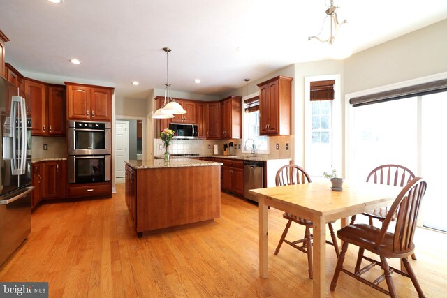 kitchen featuring pendant lighting, light wood finished floors, stainless steel appliances, a kitchen island, and light stone countertops