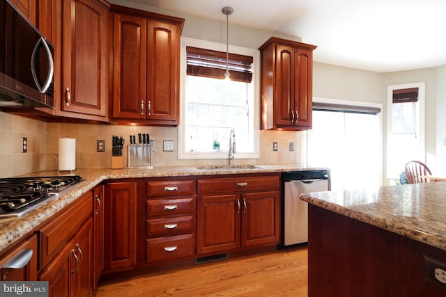 kitchen featuring light stone counters, a sink, light wood-style floors, appliances with stainless steel finishes, and decorative backsplash