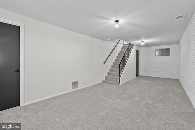 basement featuring light colored carpet and brick wall