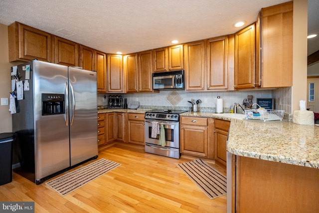 kitchen featuring sink, light stone counters, light hardwood / wood-style flooring, appliances with stainless steel finishes, and backsplash