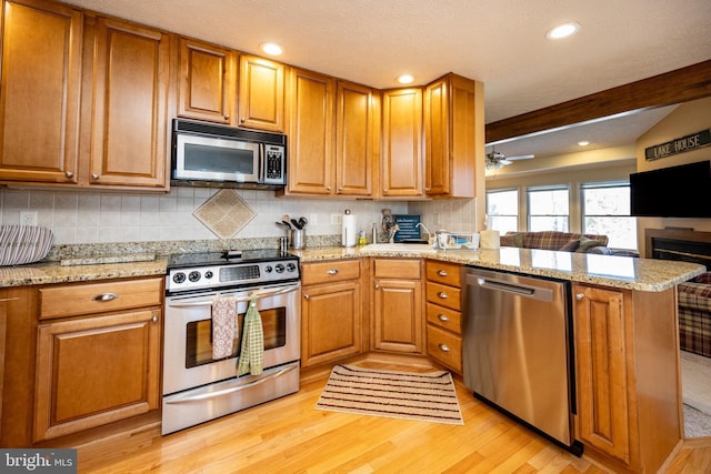 kitchen with tasteful backsplash, light stone counters, appliances with stainless steel finishes, kitchen peninsula, and light hardwood / wood-style floors