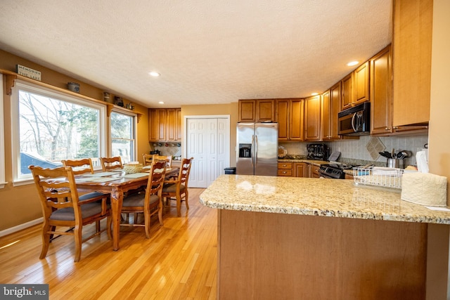 kitchen with light stone counters, light hardwood / wood-style flooring, kitchen peninsula, stainless steel appliances, and decorative backsplash