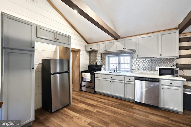 kitchen with dark wood-style floors, vaulted ceiling with beams, a sink, appliances with stainless steel finishes, and tasteful backsplash