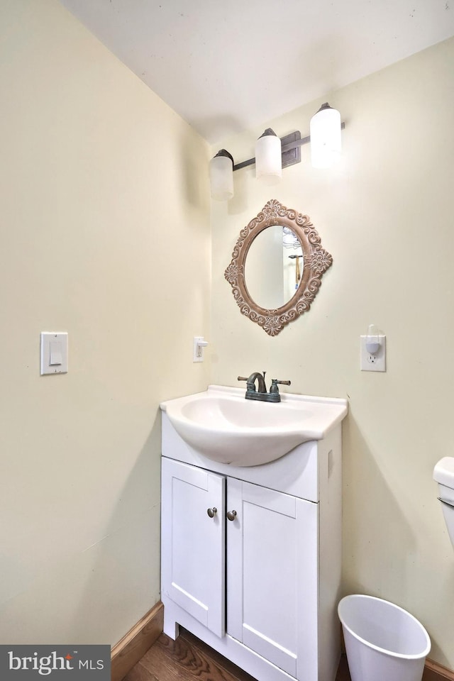 half bathroom with toilet, vanity, baseboards, and wood finished floors