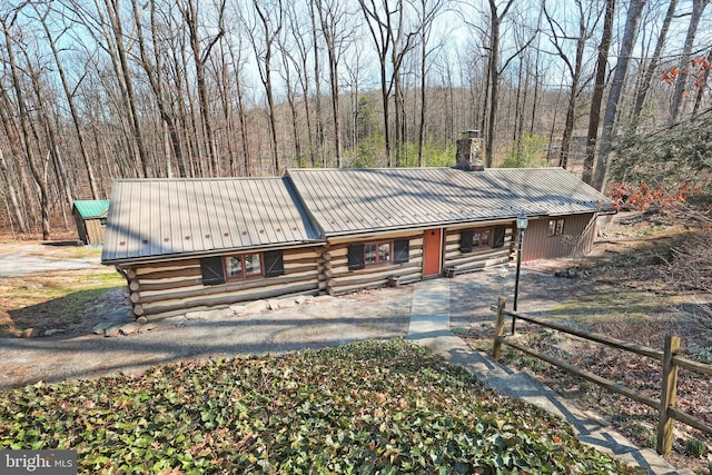 log cabin featuring log exterior, a view of trees, a chimney, and metal roof