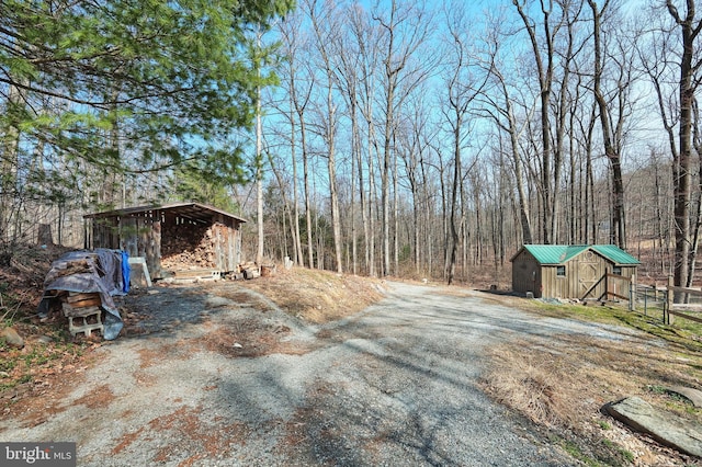 view of yard with driveway, a shed, fence, an outdoor structure, and a wooded view