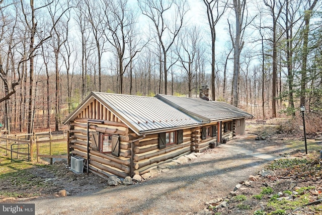 view of front facade with fence, log siding, a chimney, metal roof, and driveway