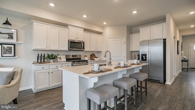 kitchen with stainless steel appliances, a kitchen bar, an island with sink, and white cabinets