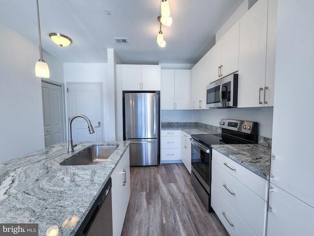 kitchen featuring hardwood / wood-style floors, sink, white cabinets, hanging light fixtures, and stainless steel appliances