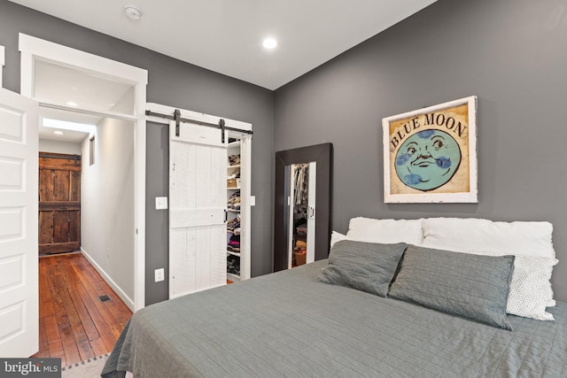 bedroom with wood-type flooring, a barn door, and a spacious closet