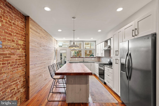 kitchen with appliances with stainless steel finishes, white cabinetry, a kitchen bar, hanging light fixtures, and a center island