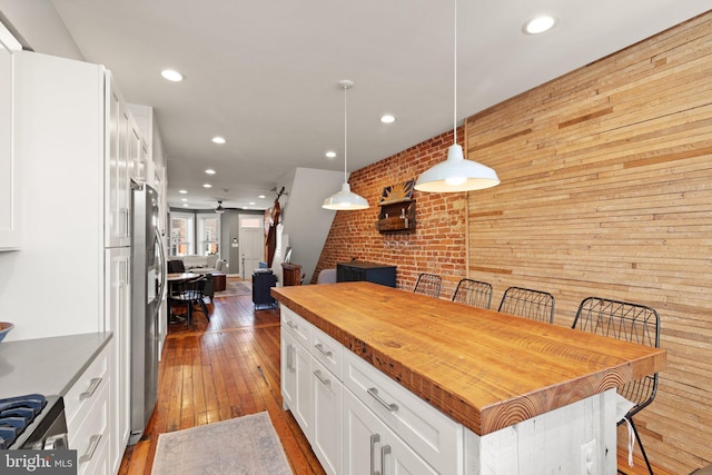 kitchen featuring decorative light fixtures, a breakfast bar area, white cabinets, a center island, and stainless steel refrigerator with ice dispenser