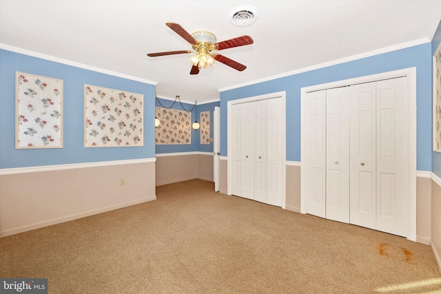 unfurnished bedroom featuring multiple closets, ceiling fan, crown molding, and carpet