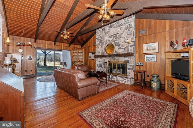 living room featuring ceiling fan, hardwood / wood-style floors, beam ceiling, a fireplace, and wood walls